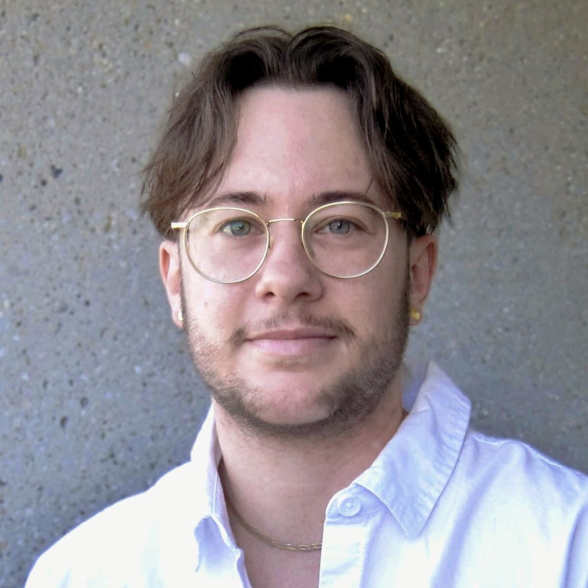 Portrait von Monet Wohlgemuth, er ist eine weisse Person mit braunen Haaren und einem leichten Bart. Er schaut direkt in die Kamera und trägt ein weisses Hemd und eine Brille.